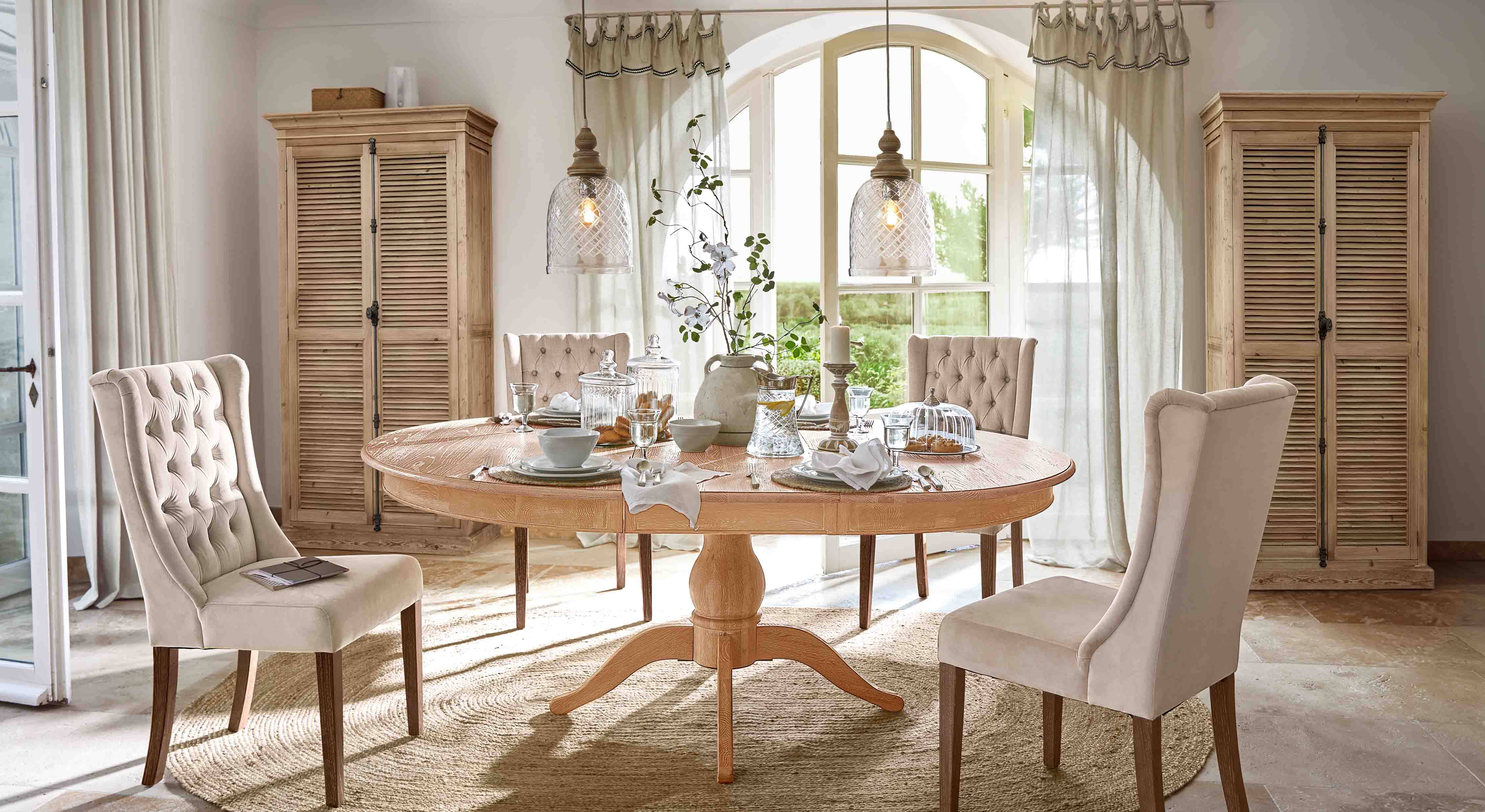 Sala da pranzo con tavolo rotondo in legno chiaro e sedie imbottite beige in stile classico