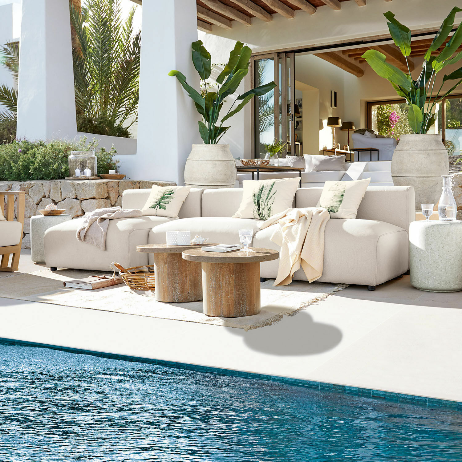 Divano modulare Vézère Divano beige in tessuto su terrazza vicino alla piscina con tavolini in legno e cuscini decorativi