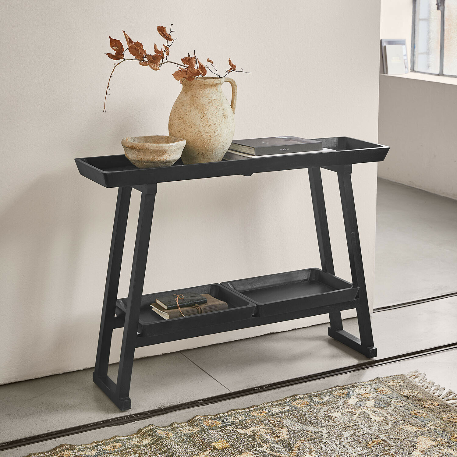 Consolle Ivywood Tavolino nero in legno con ripiani, vaso in ceramica e libri in interno minimalista