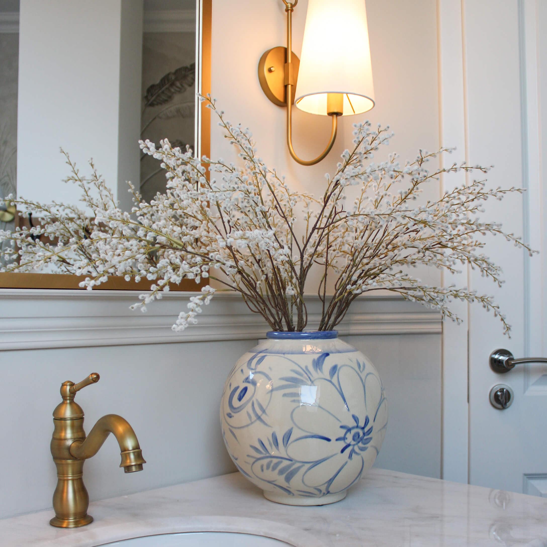 Vaso in ceramica con motivo floreale blu e rami di fiori bianchi su piano in marmo in bagno