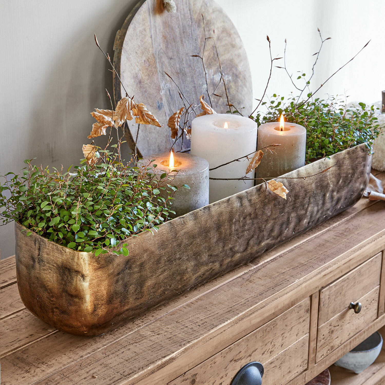 Centrotavola Skye Fioriera decorativa in metallo dorato con piante verdi e tre candele su tavolo in legno