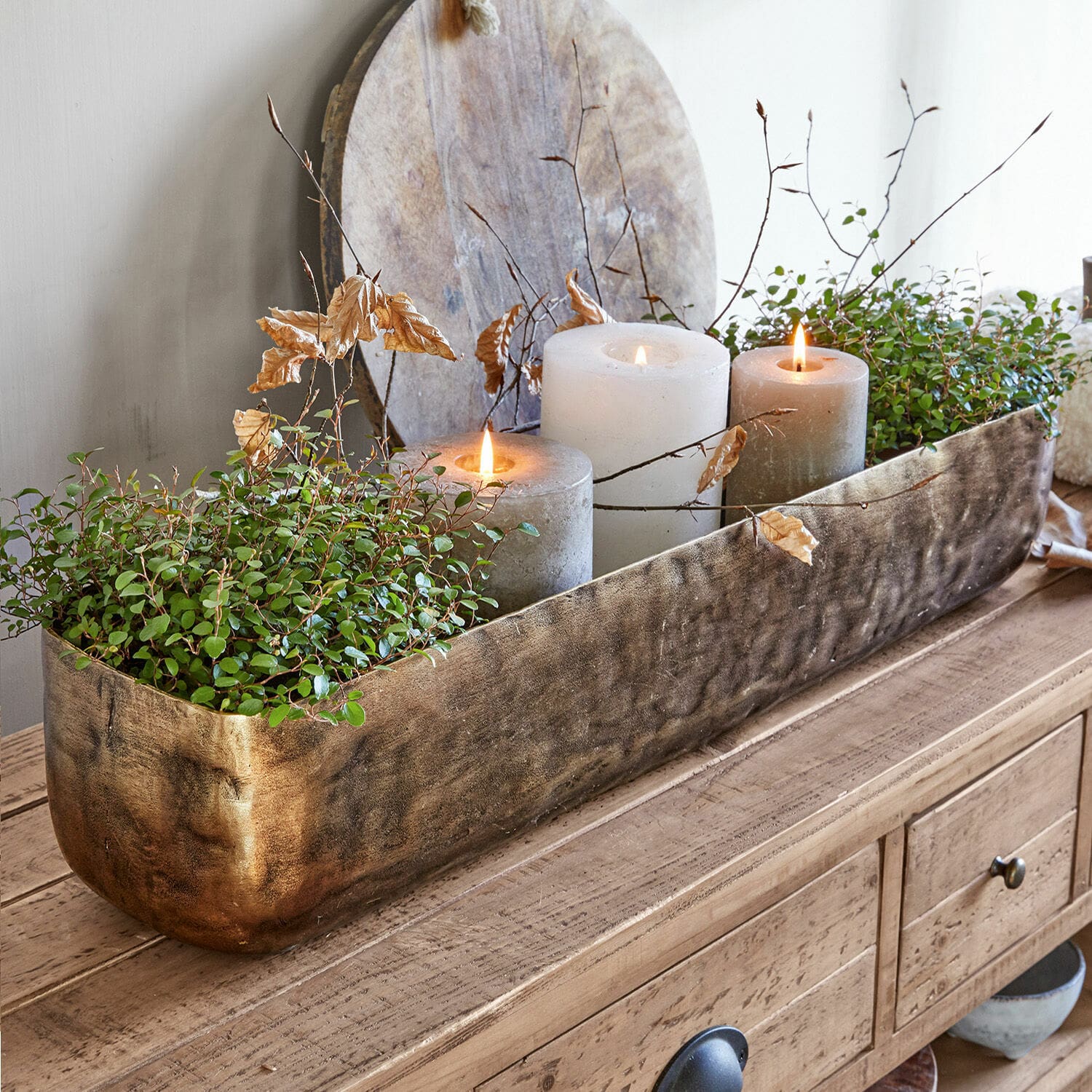 Centrotavola Skye Fioriera decorativa in metallo dorato con piante verdi e tre candele su tavolo in legno