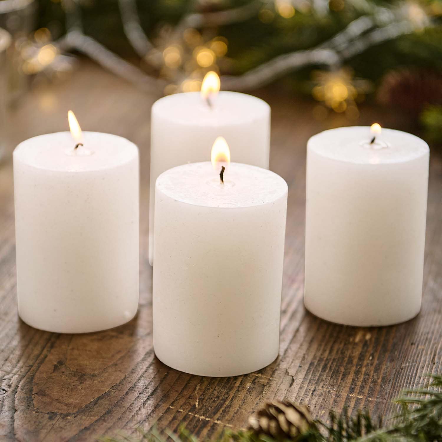 Set di quattro candele bianche cilindriche accese su tavolo in legno con decorazioni natalizie