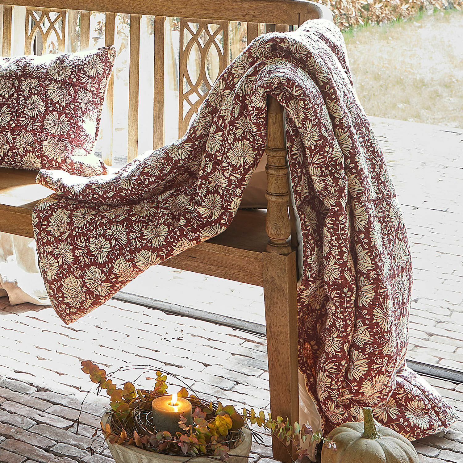 Trapunta Soleique Coperta e cuscino rossi con motivo floreale su panca in legno, decorazione autunnale con zucca e candela