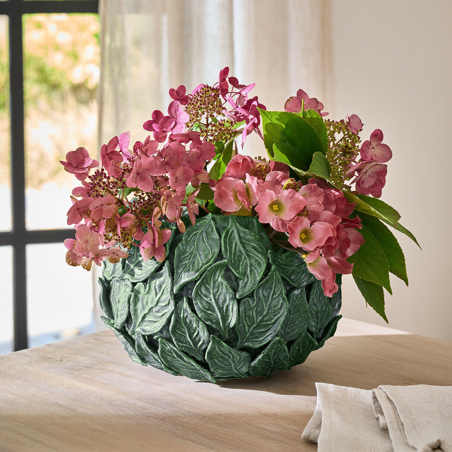 Vaso decorativo verde a forma di foglie con fiori rosa su tavolo in legno in ambiente luminoso
