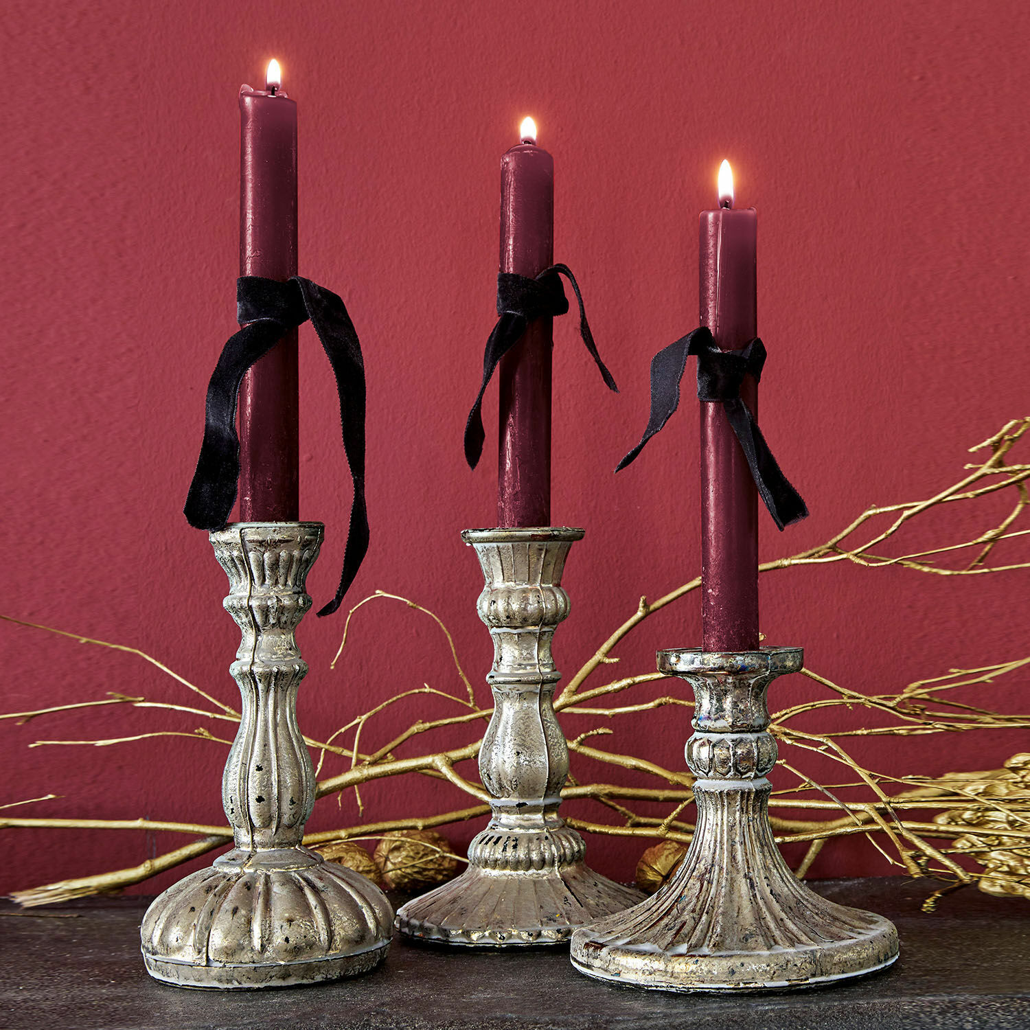 Set di 3 candelieri Bretagne Tre portacandele in metallo decorativo con candele bordeaux e nastri neri su sfondo scuro