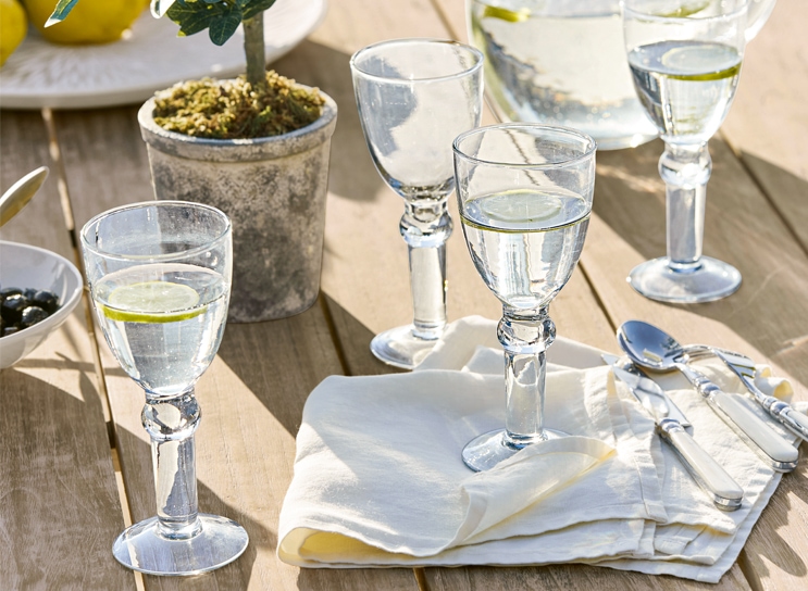 Bicchieri d'acqua con limone su tavolo in legno con tovagliolo bianco e posate, stile mediterraneo