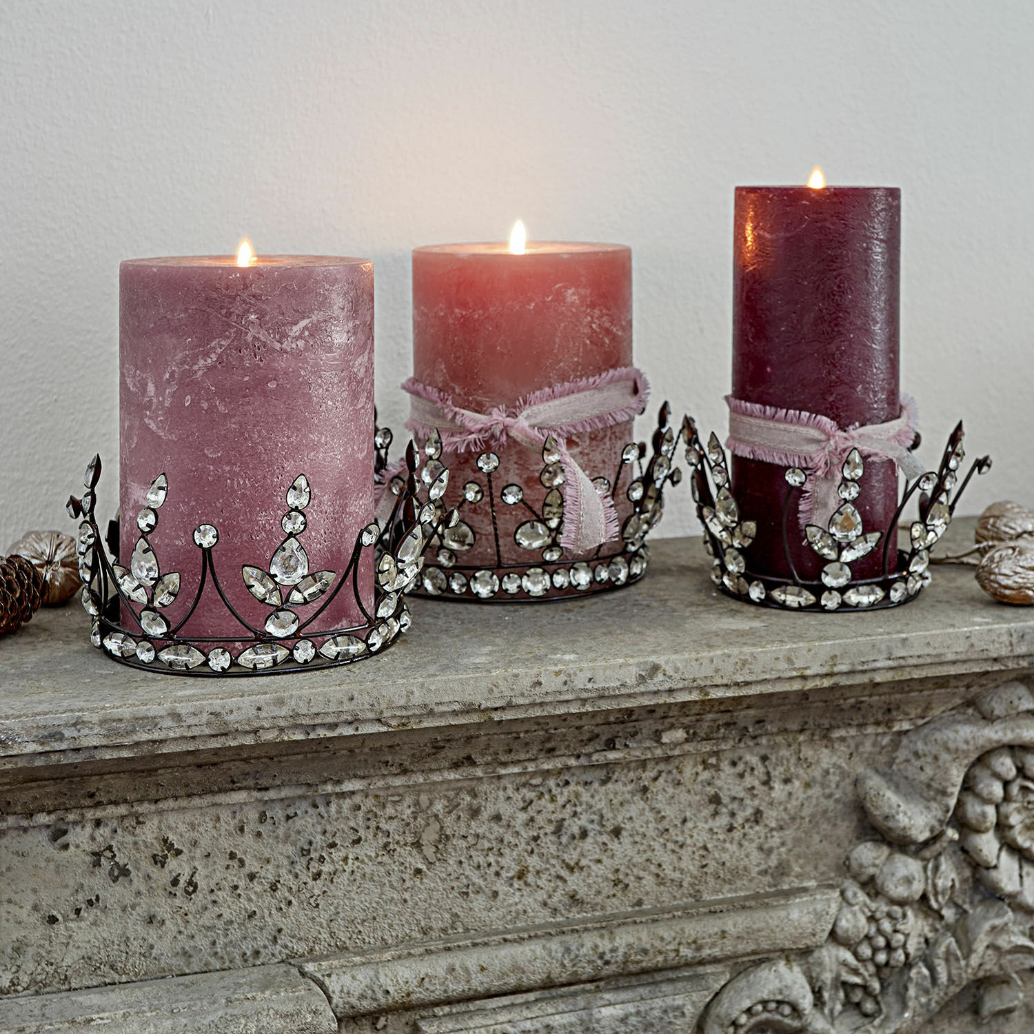Set di 3 coroncine decorative Bigas Tre candele decorative rosa con basi metalliche decorate con cristalli su un camino in pietra