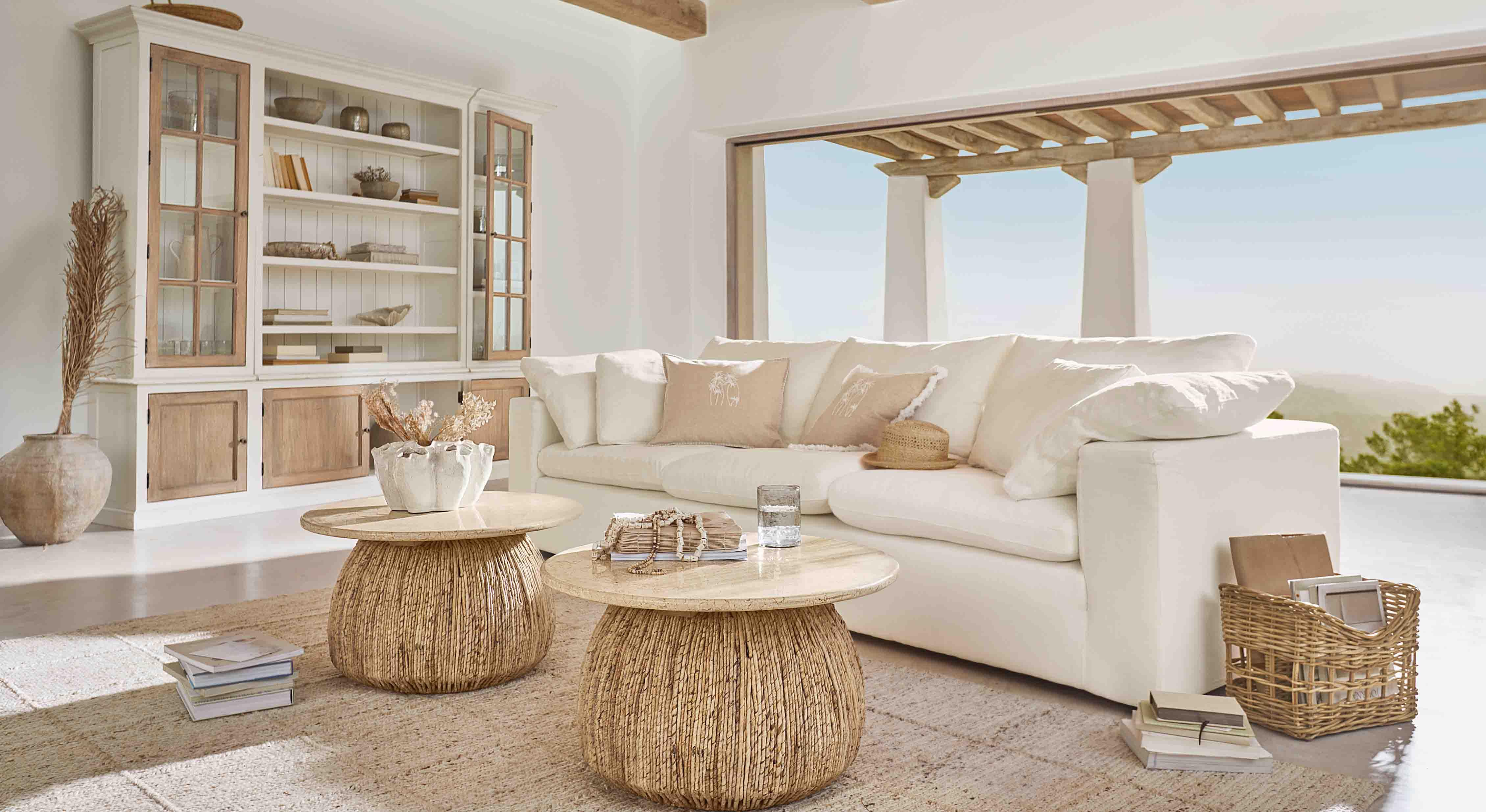 Soggiorno accogliente con divano bianco e due tavolini rotondi in legno naturale e rattan
