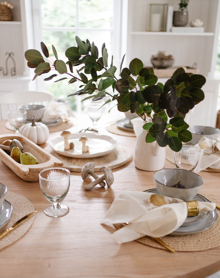 Tavola autunnale in legno chiaro con decorazioni di foglie, funghi e stoviglie eleganti per pranzo