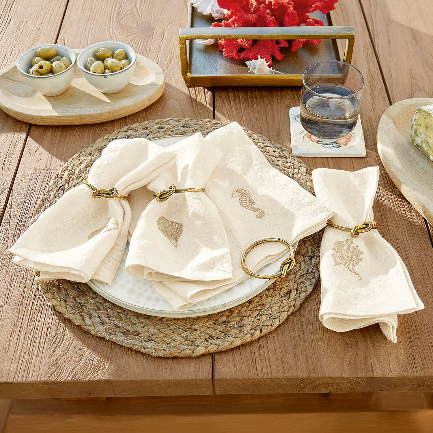 Tovaglioli in lino crema con motivi marini e anelli dorati su tavolo in legno per decorazione tavola