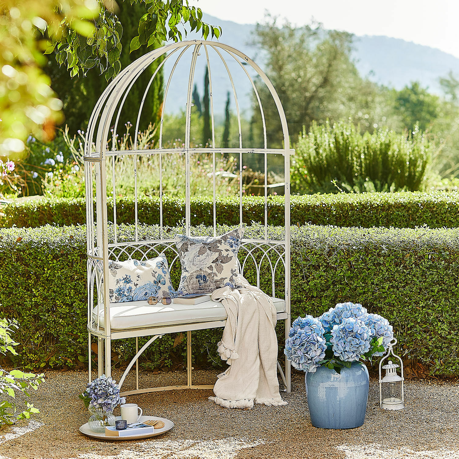 Panchina Rivandelle Panca da giardino in metallo bianco con cuscini e coperta, decorata con fiori di ortensia blu