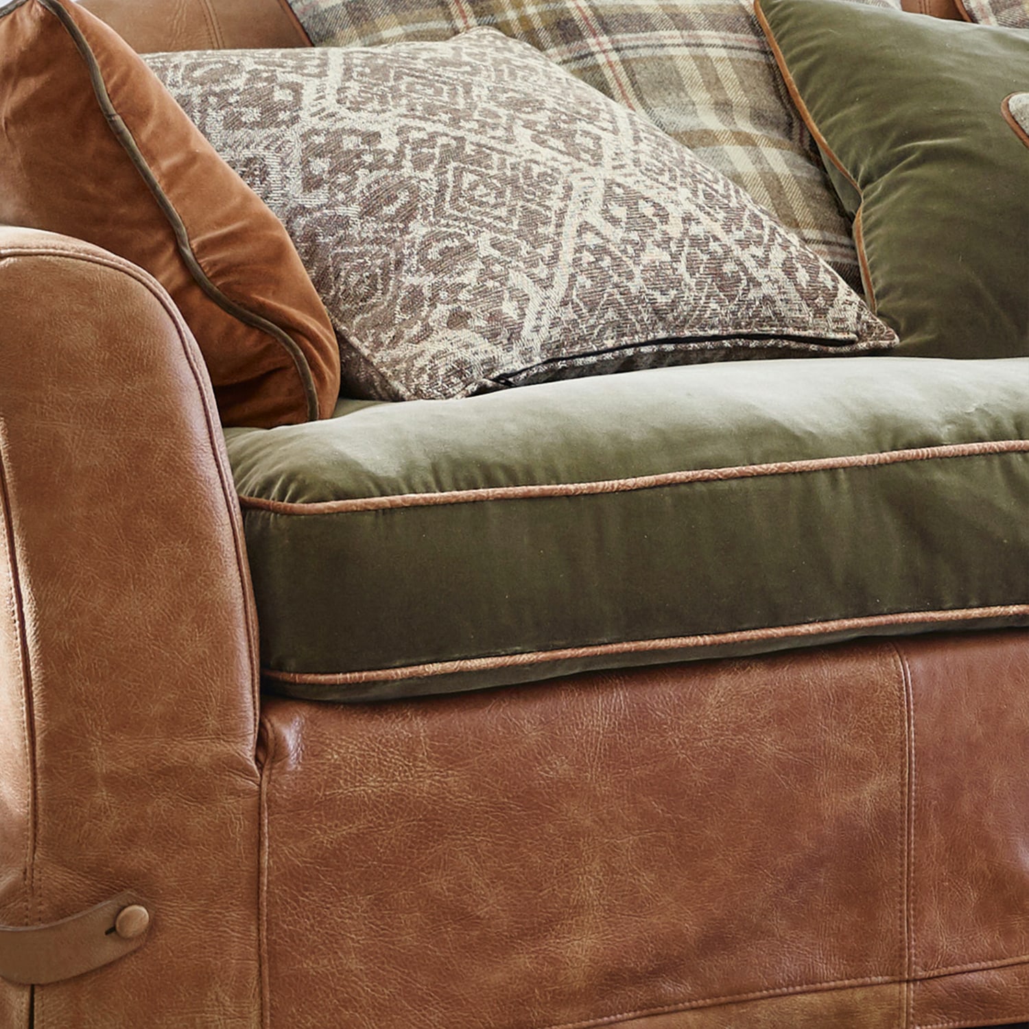 Divano in pelle marrone con seduta in velluto verde e cuscini decorativi in stile rustico