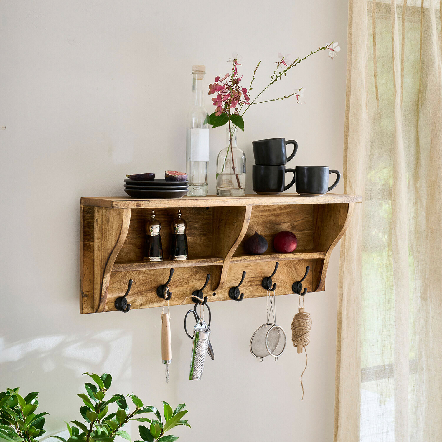 Mensola da parete in legno con ganci, tazze nere, piatti e decorazione floreale in interno luminoso