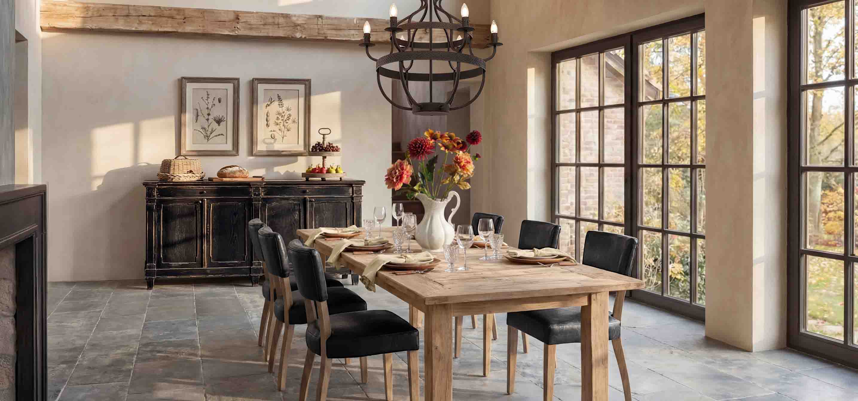 Sala da pranzo con tavolo in legno, sedie nere e credenza rustica davanti a grandi finestre