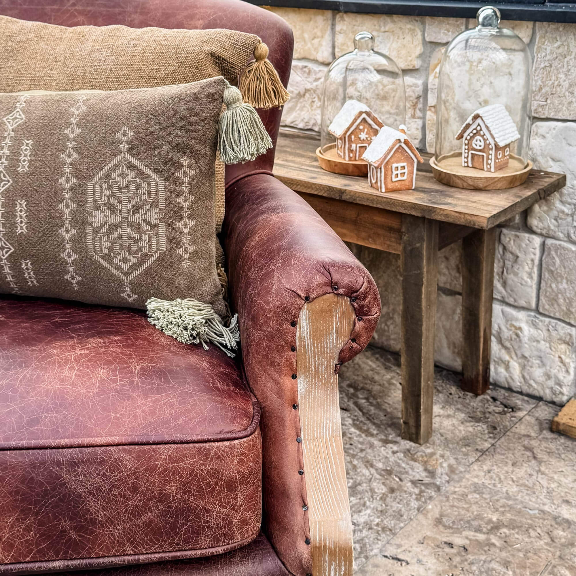 Divano in pelle marrone con cuscini decorativi e tavolo in legno con casette di pan di zenzero natalizie