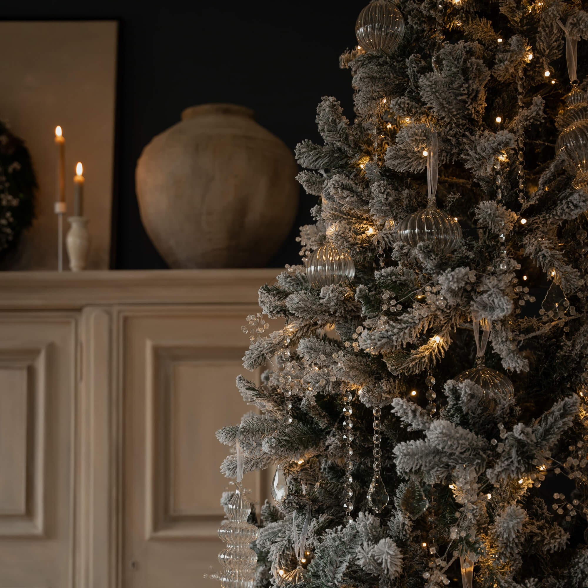 Albero di Natale innevato con decorazioni in vetro trasparente e luci calde in un ambiente accogliente