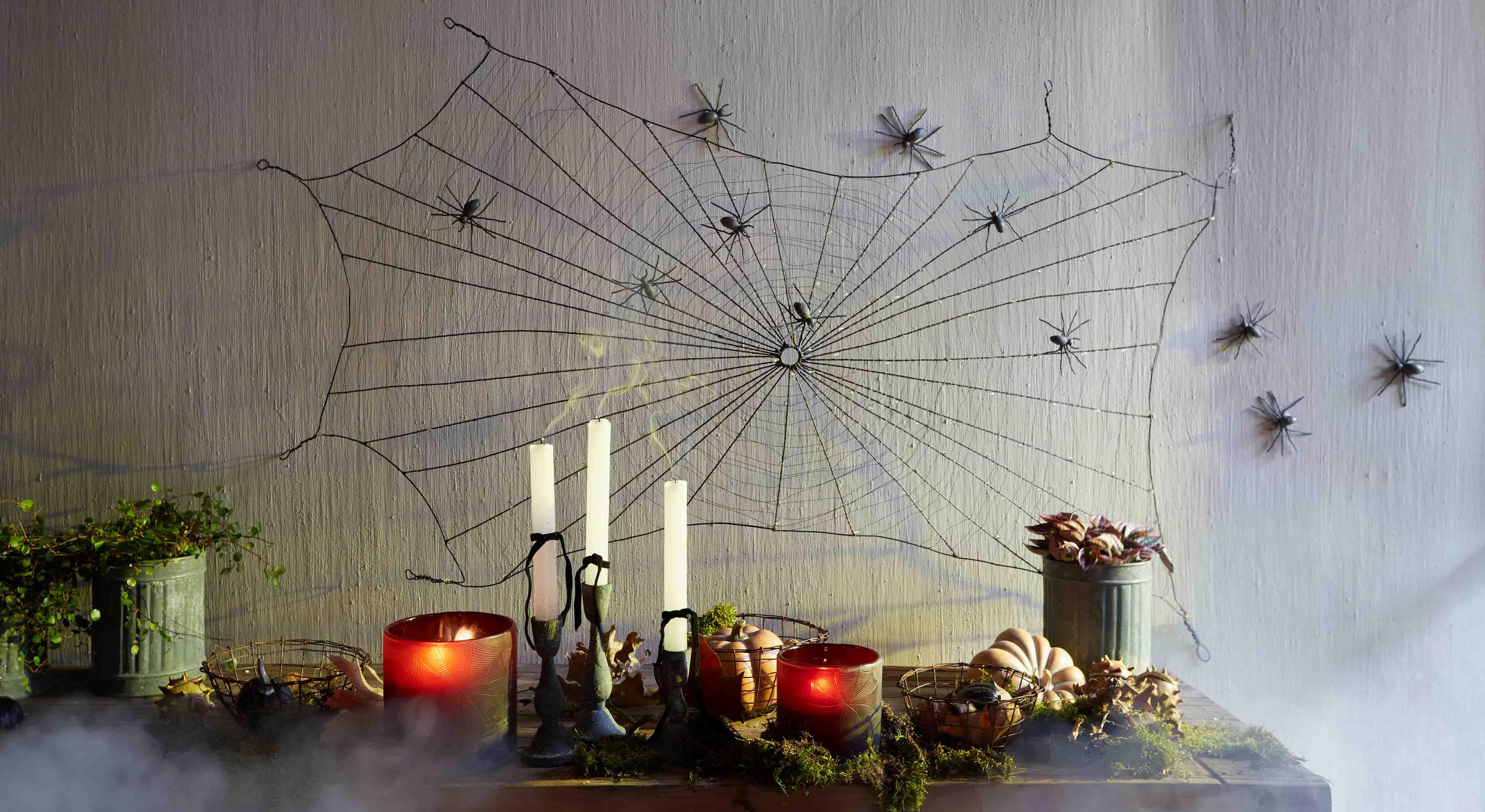Decorazione di Halloween con ragnatela nera e ragni di plastica sul muro, candele e zucche sul tavolo