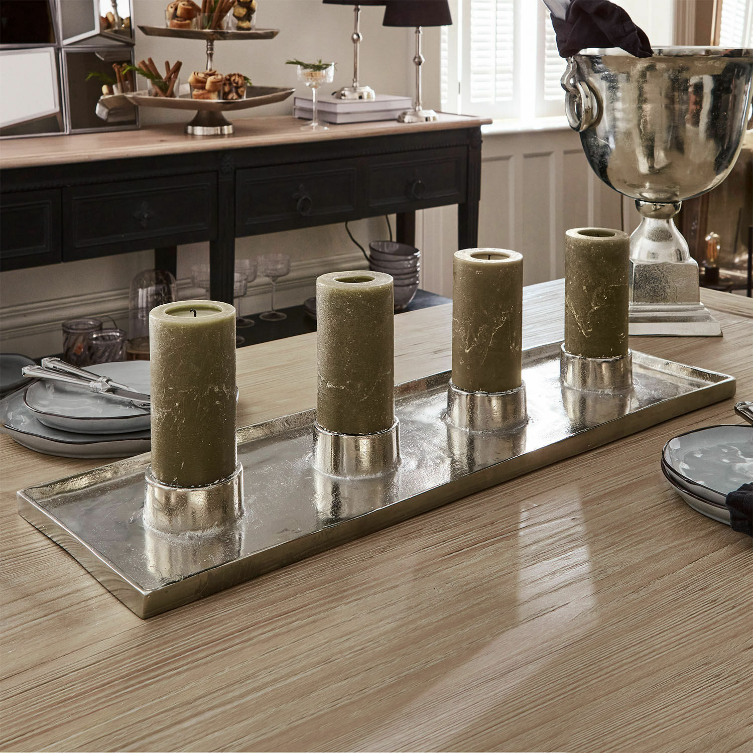 Set di quattro candele verdi su vassoio metallico argentato su tavolo in legno in sala da pranzo