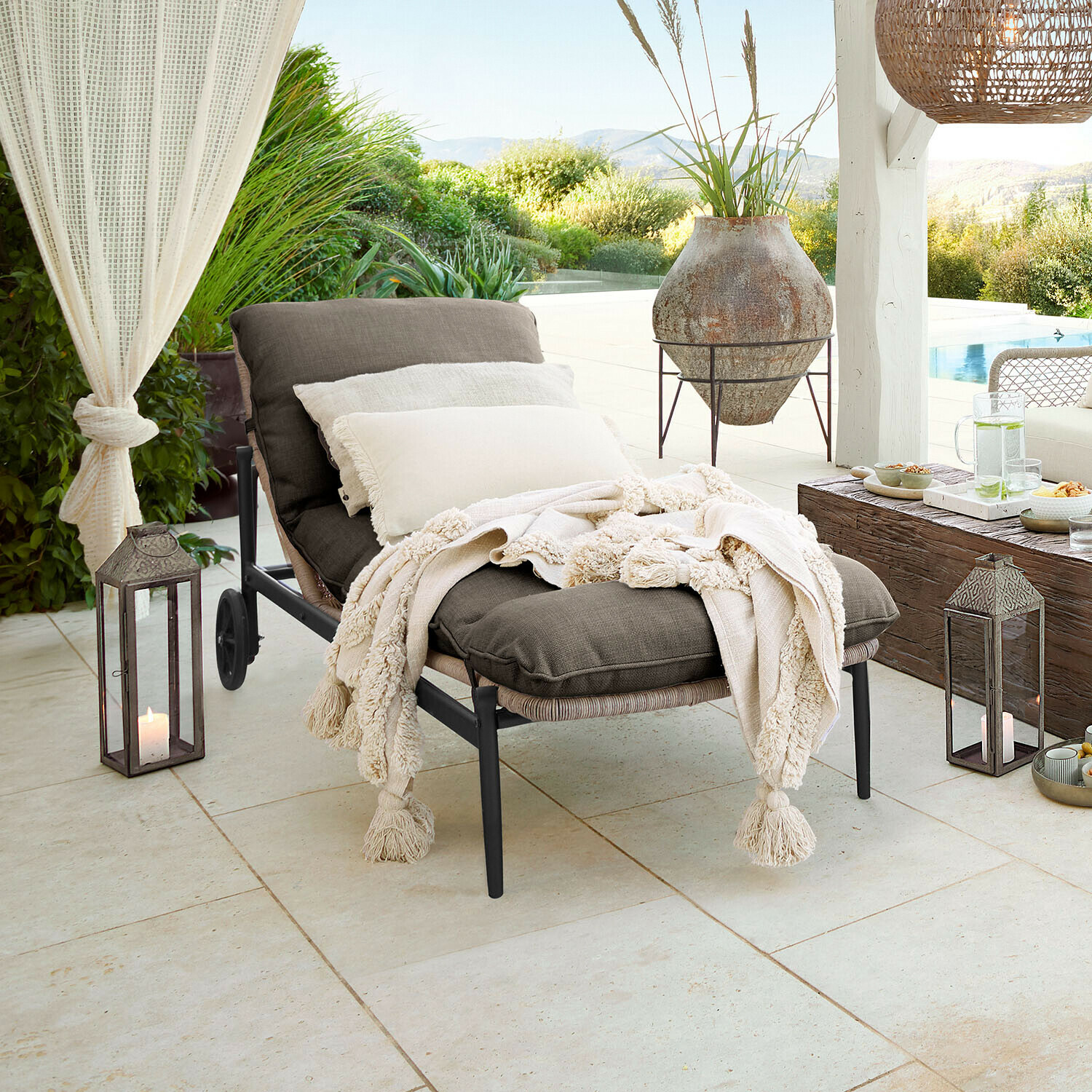 Lettino Langforda Lettino da giardino con tessuto grigio scuro e coperta crema con frange su terrazza con vista giardino