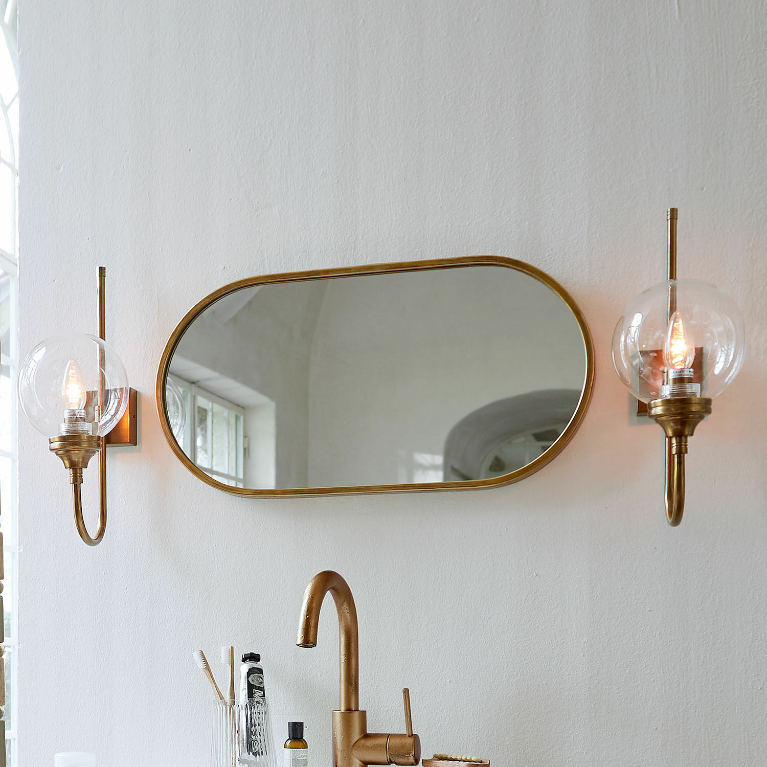 Specchio Anthé Specchio ovale con cornice in ottone e due applique da parete con paralumi trasparenti in bagno
