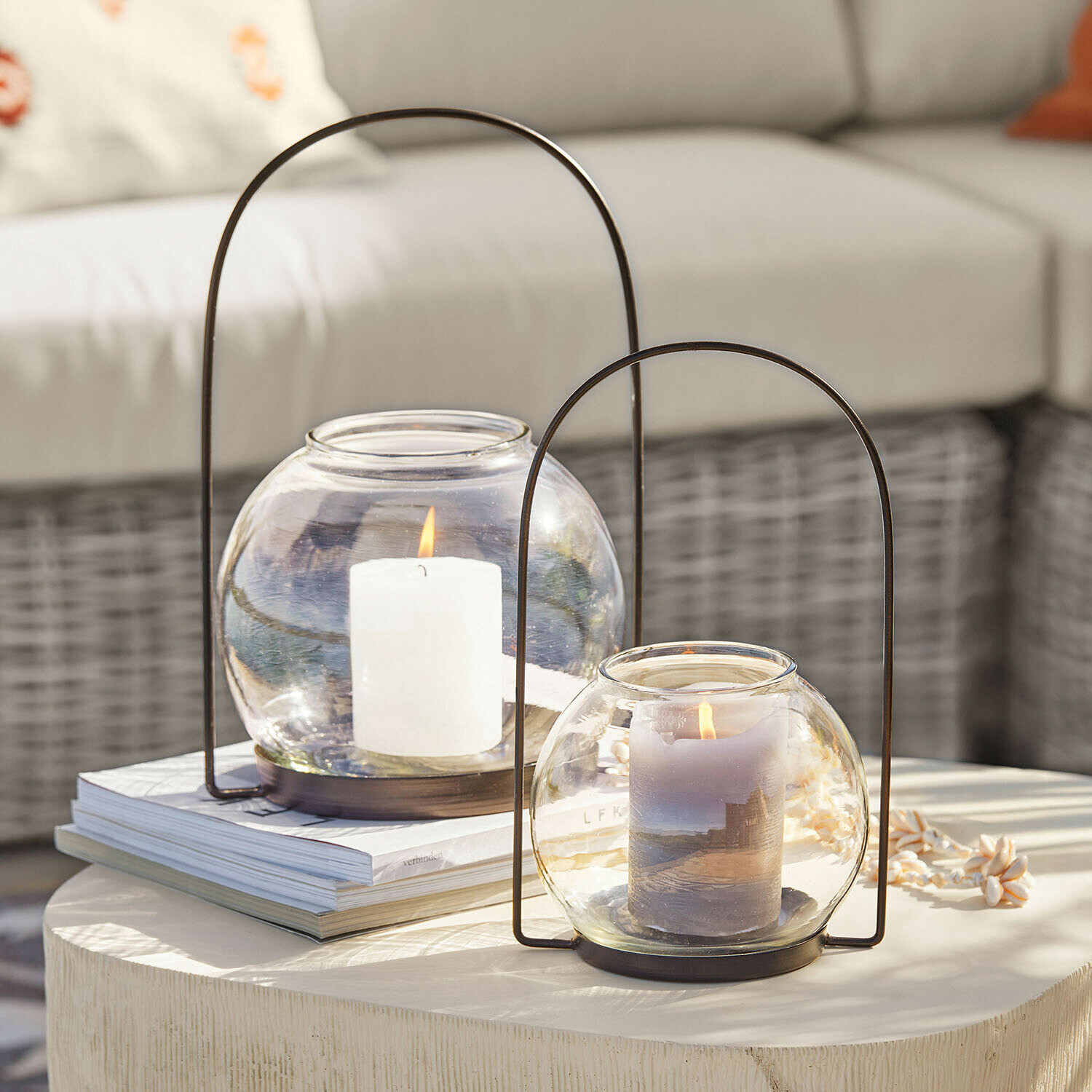 Coppia di lanterne Serenaro Due lanterne in vetro con manici in metallo e candele accese su un tavolo decorativo chiaro