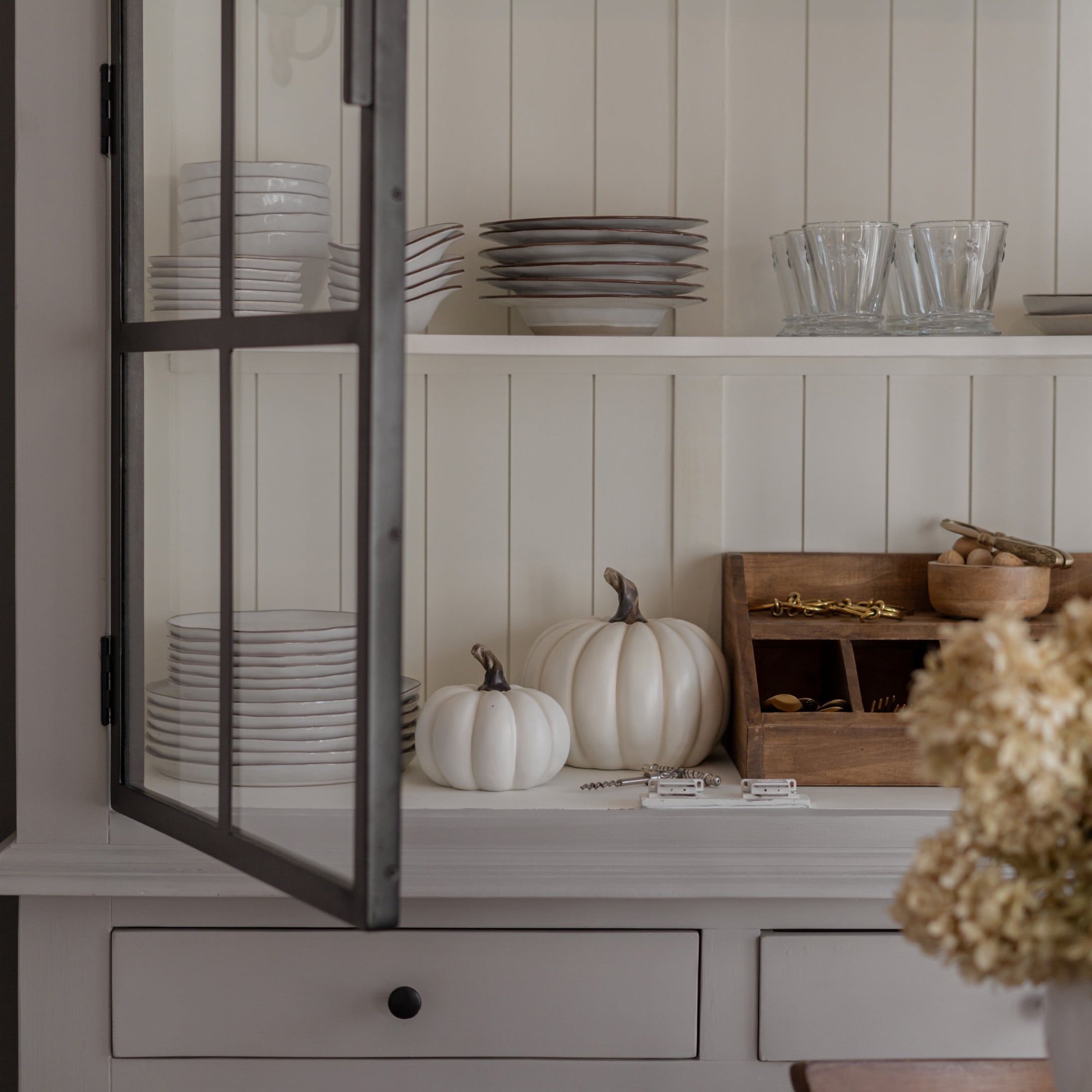 Piatti bianchi in ceramica e bicchieri su mensola con zucche bianche decorative e organizer in legno