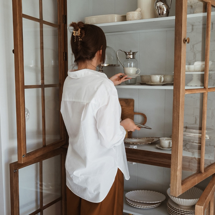 Donna con camicia bianca prende tazza di porcellana da vetrina in legno con stoviglie