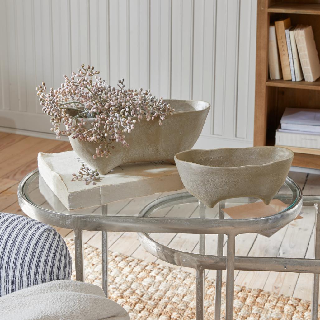 Due ciotole beige in ceramica con piedini su tavolo in vetro in un interno luminoso e accogliente