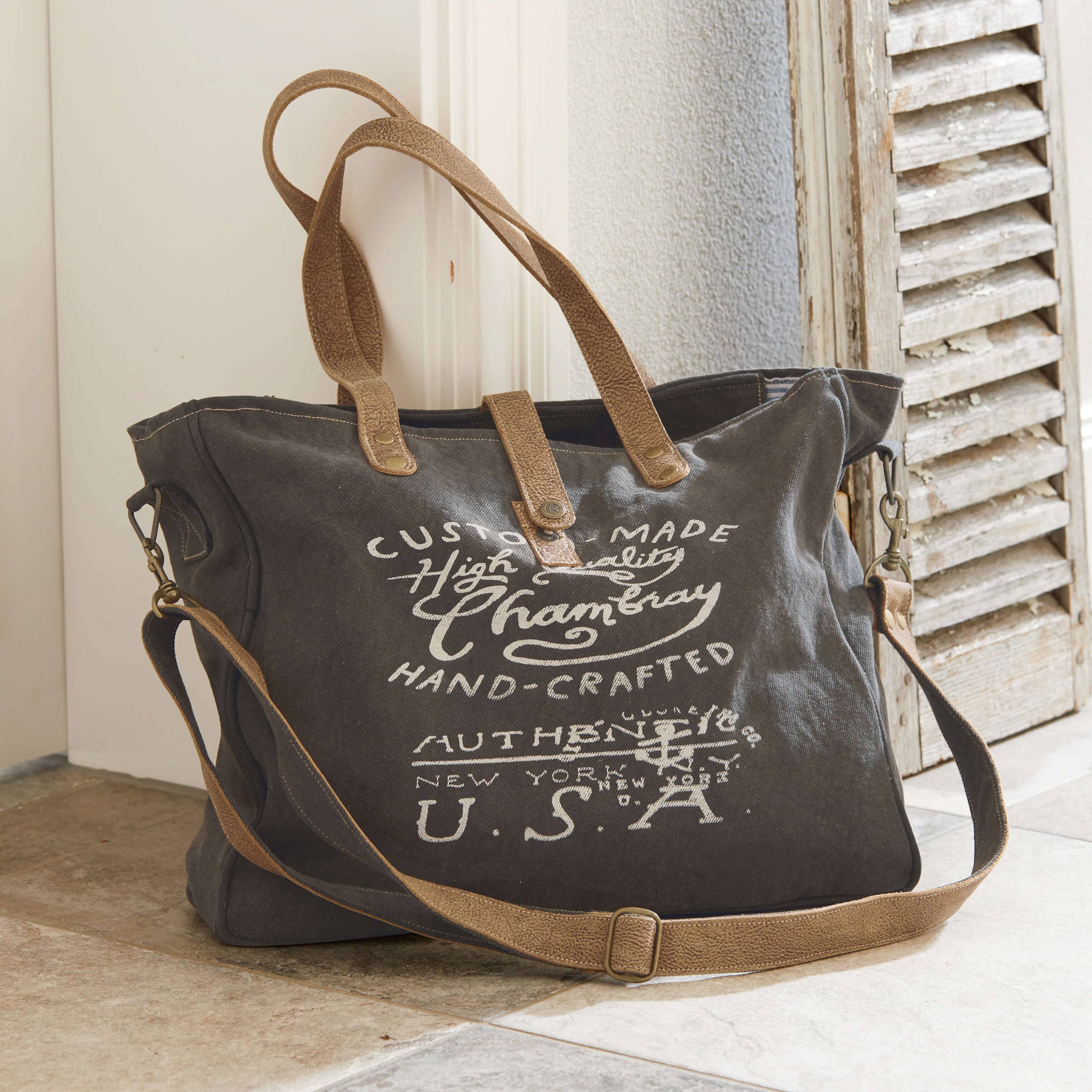 Borsa da viaggio in tessuto grigio scuro con manici in pelle marrone e stampa testuale bianca