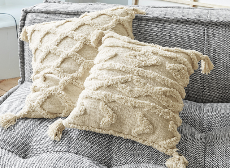 Cuscini decorativi beige con frange e motivo geometrico su divano grigio in tessuto