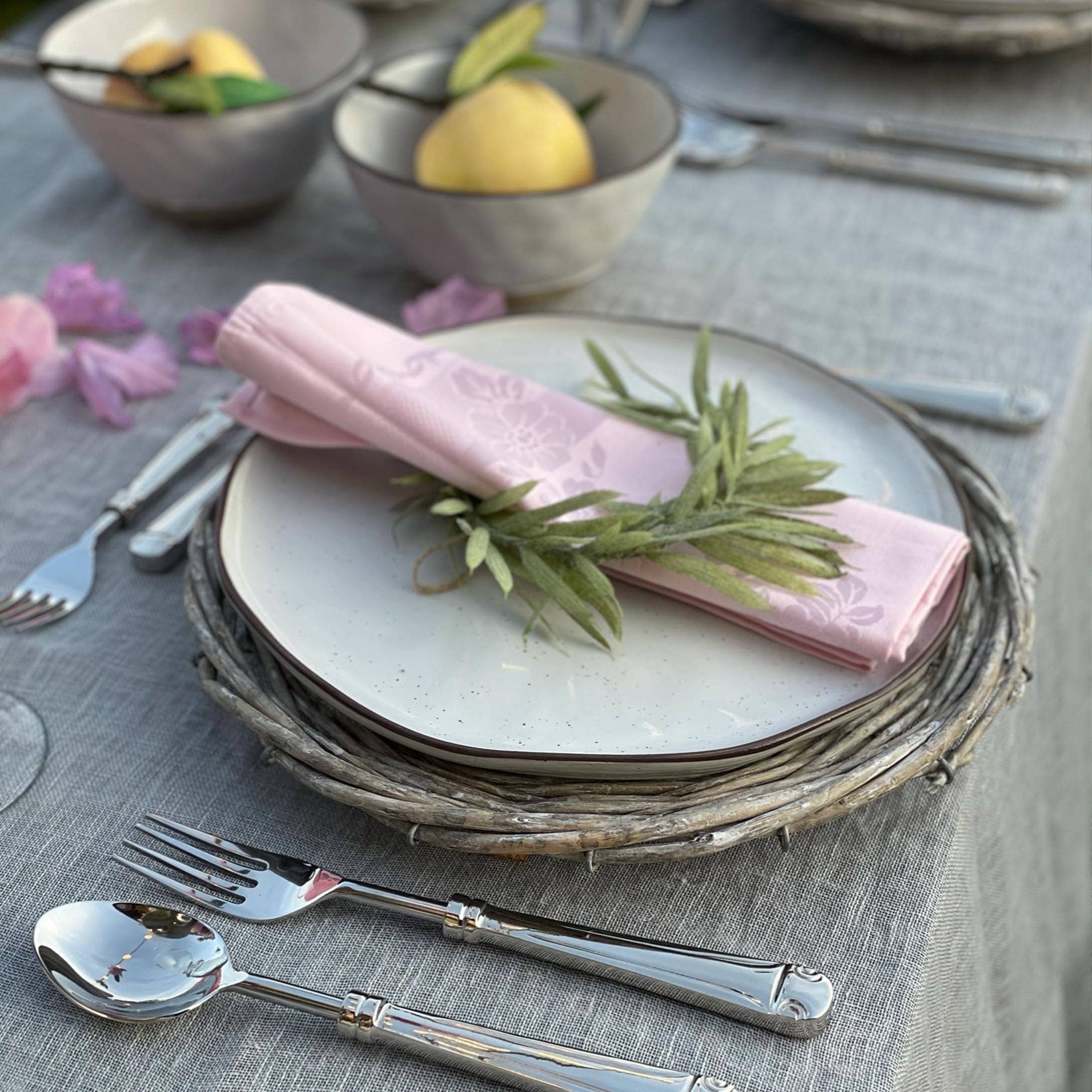 Elegante apparecchiatura con piatto bianco su sottopiatto in vimini e tovagliolo rosa con foglie verdi