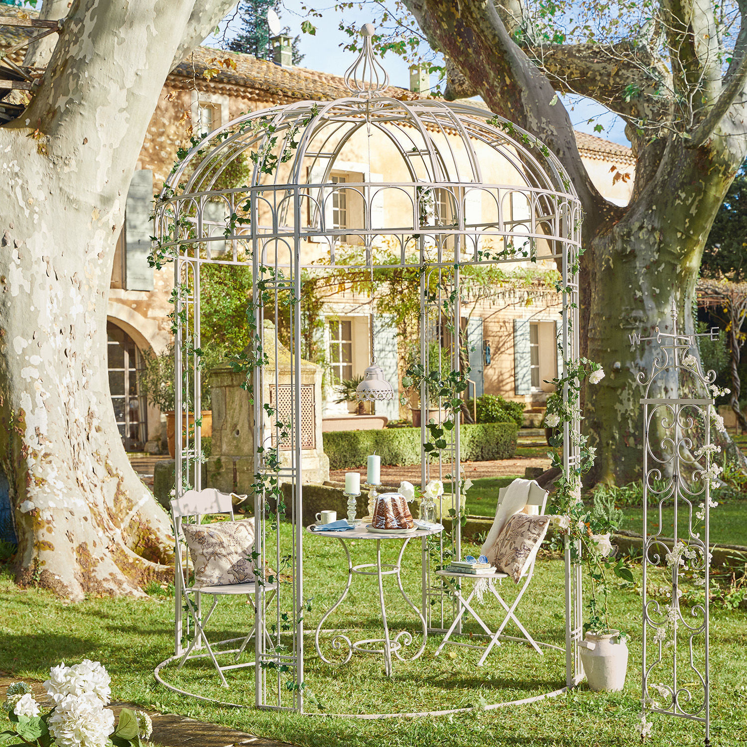 Gazebo Iolanda Gazebo da giardino in metallo bianco con sedie e tavolo su prato, decorato con edera verde