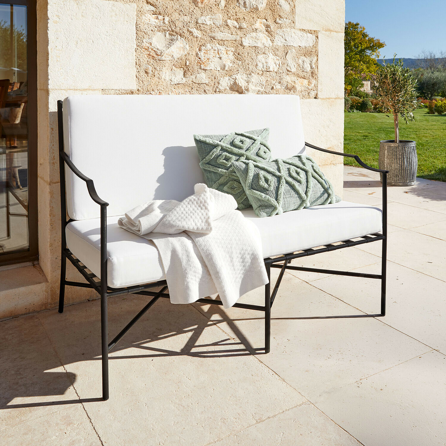 Divano Vexford Panca da giardino in metallo bianco con cuscini morbidi e cuscini decorativi verdi su terrazza soleggiata