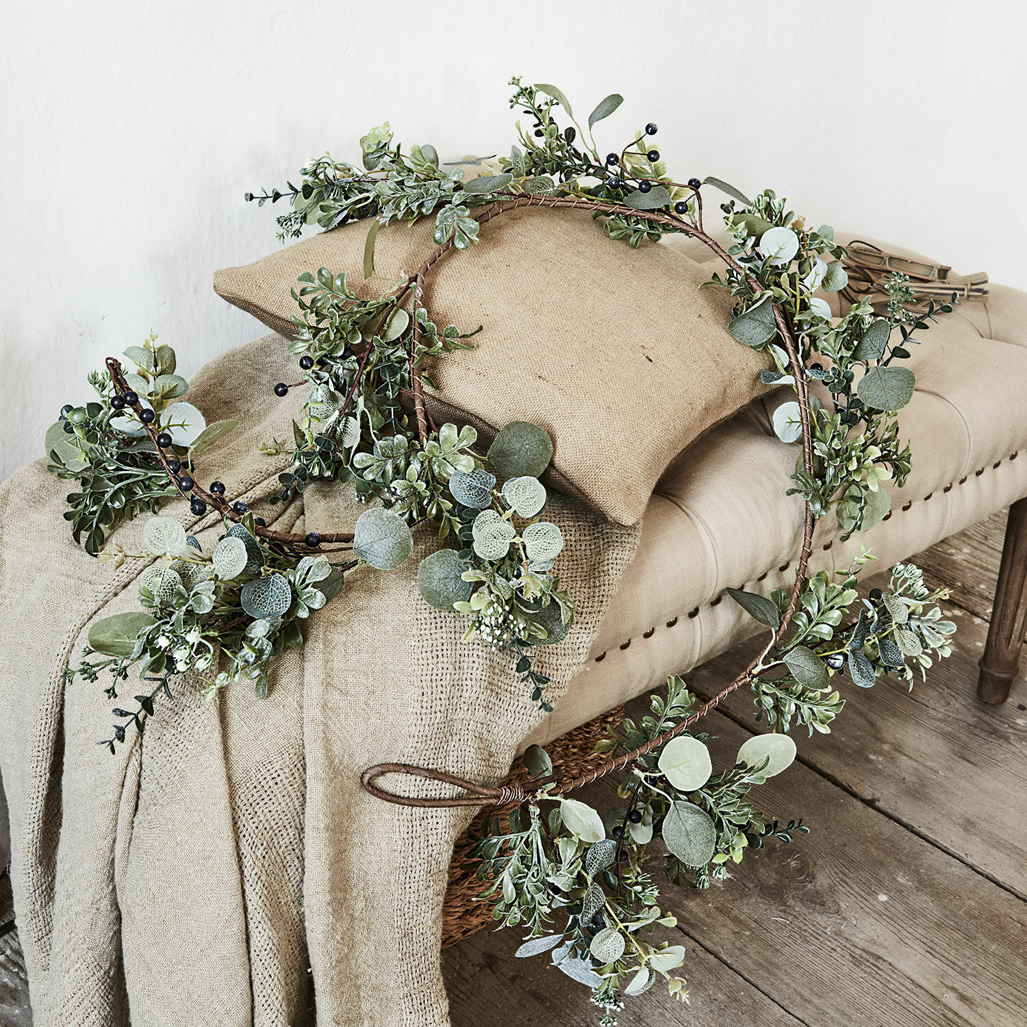 Festone Grand Corona decorativa con foglie verdi e bacche nere su tessuto beige e panca in legno
