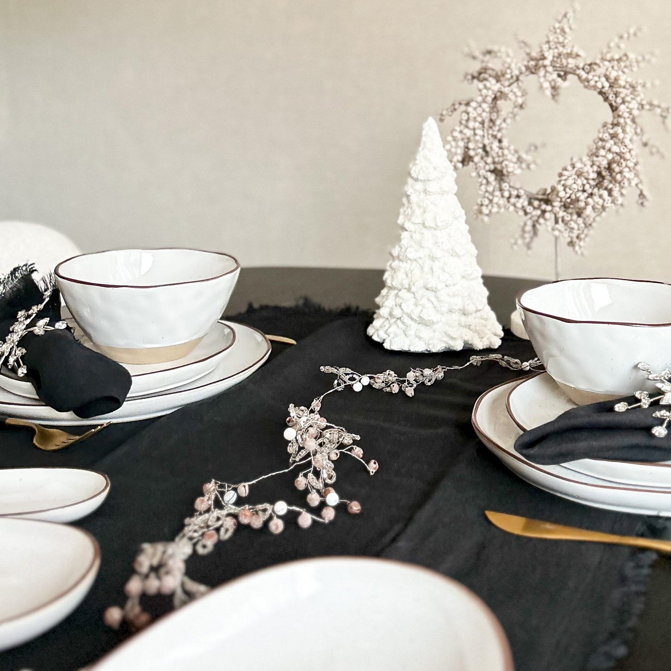 Servizio di piatti in ceramica bianca con bordo marrone su tovaglia nera con decorazioni natalizie