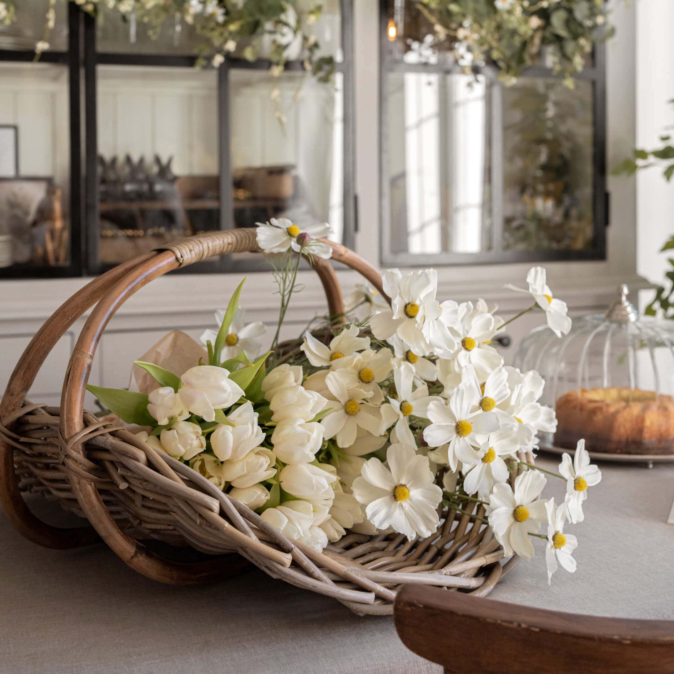 Cesto di vimini con tulipani bianchi e fiori decorativi su tavolo in ambiente luminoso