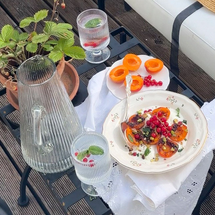 Caraffa e due bicchieri di vetro con acqua alla menta su tavolo con piatti di albicocche e ribes rossi