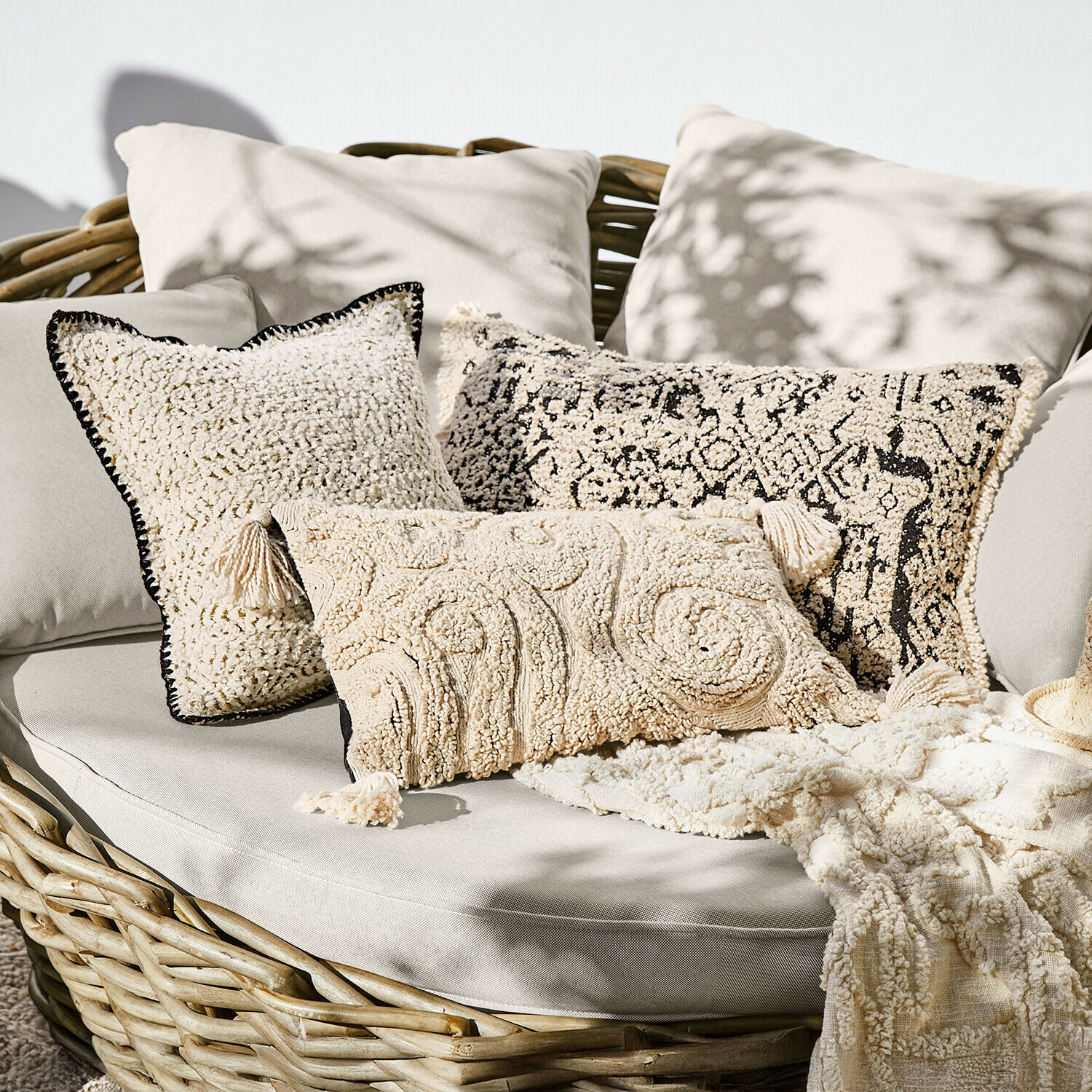 Set di cuscini decorativi crema in materiale morbido su divano in vimini, stile boho