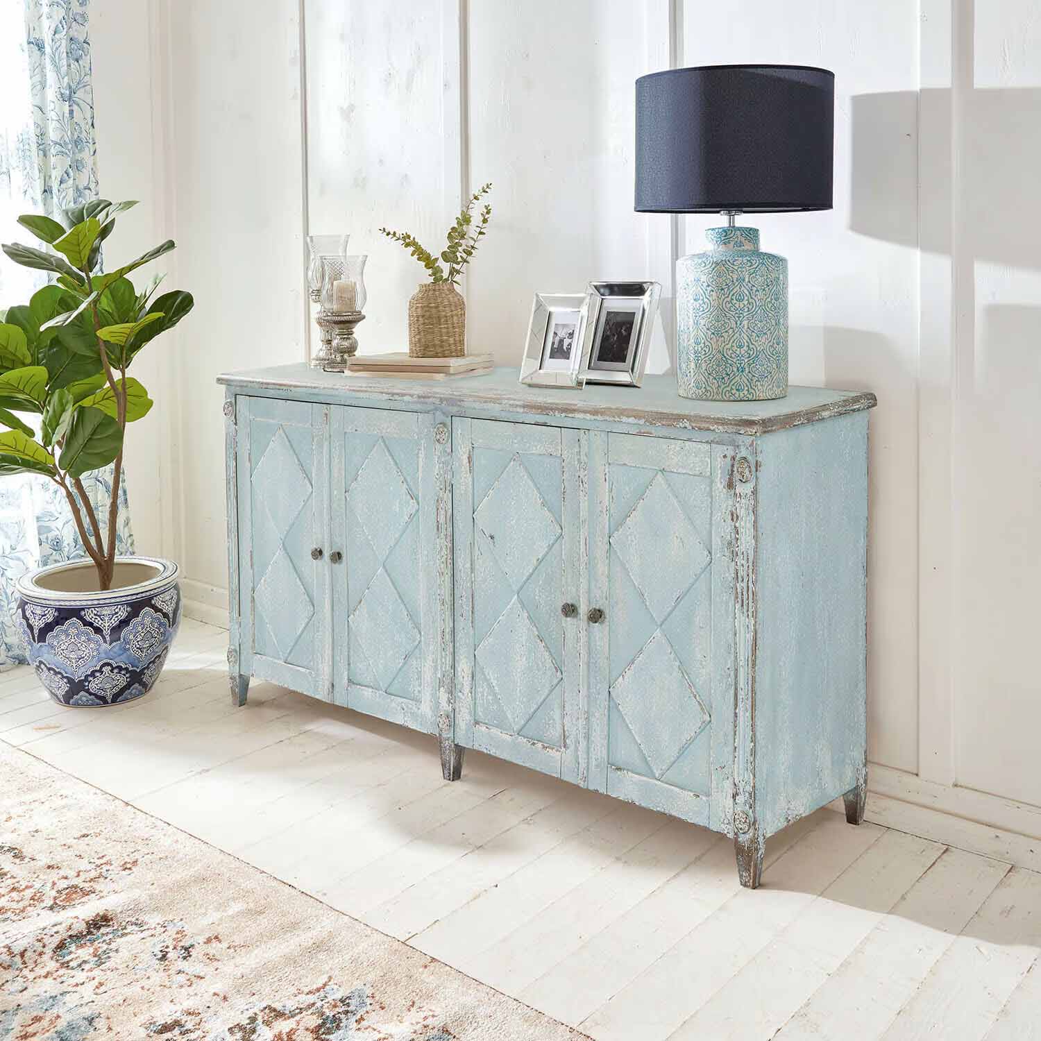 Credenza in legno blu effetto vintage in ambiente luminoso con lampada e pianta decorativa