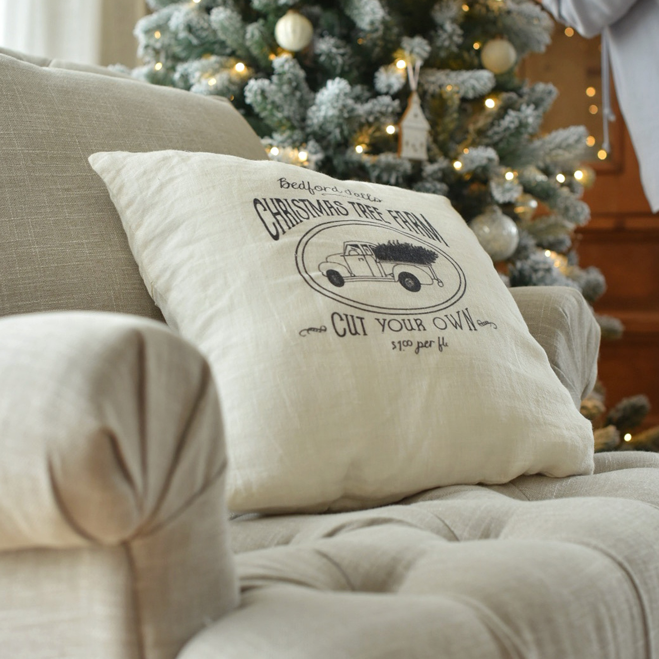 Cuscino beige in lino con stampa di camion natalizio su divano vicino ad albero di Natale decorato