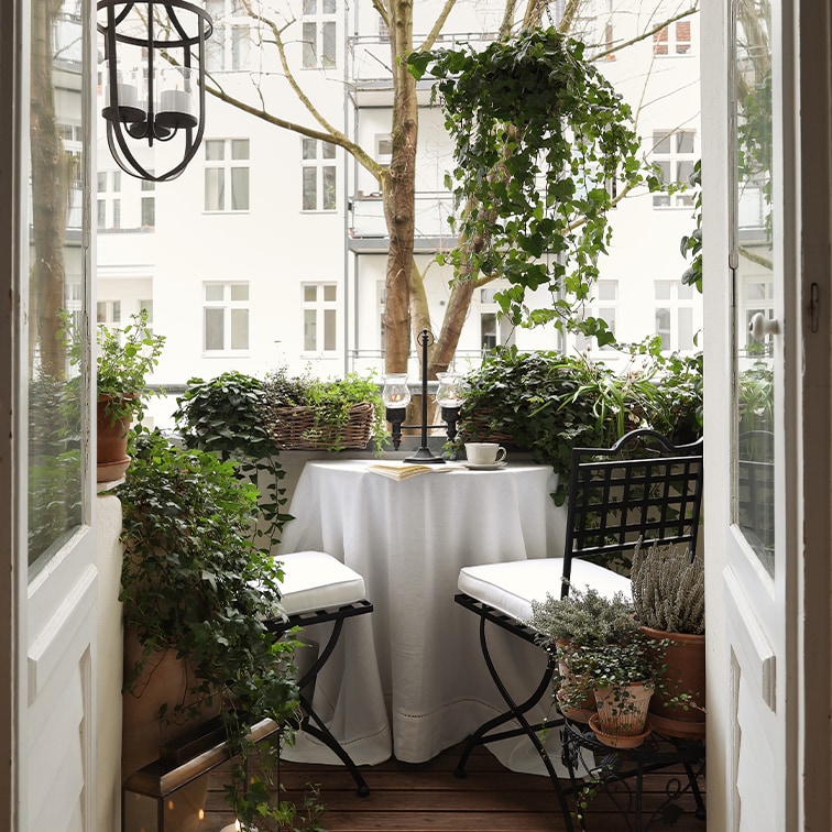 Balcone accogliente con tavolo bianco, sedie nere e piante verdi, ideale per rilassarsi.