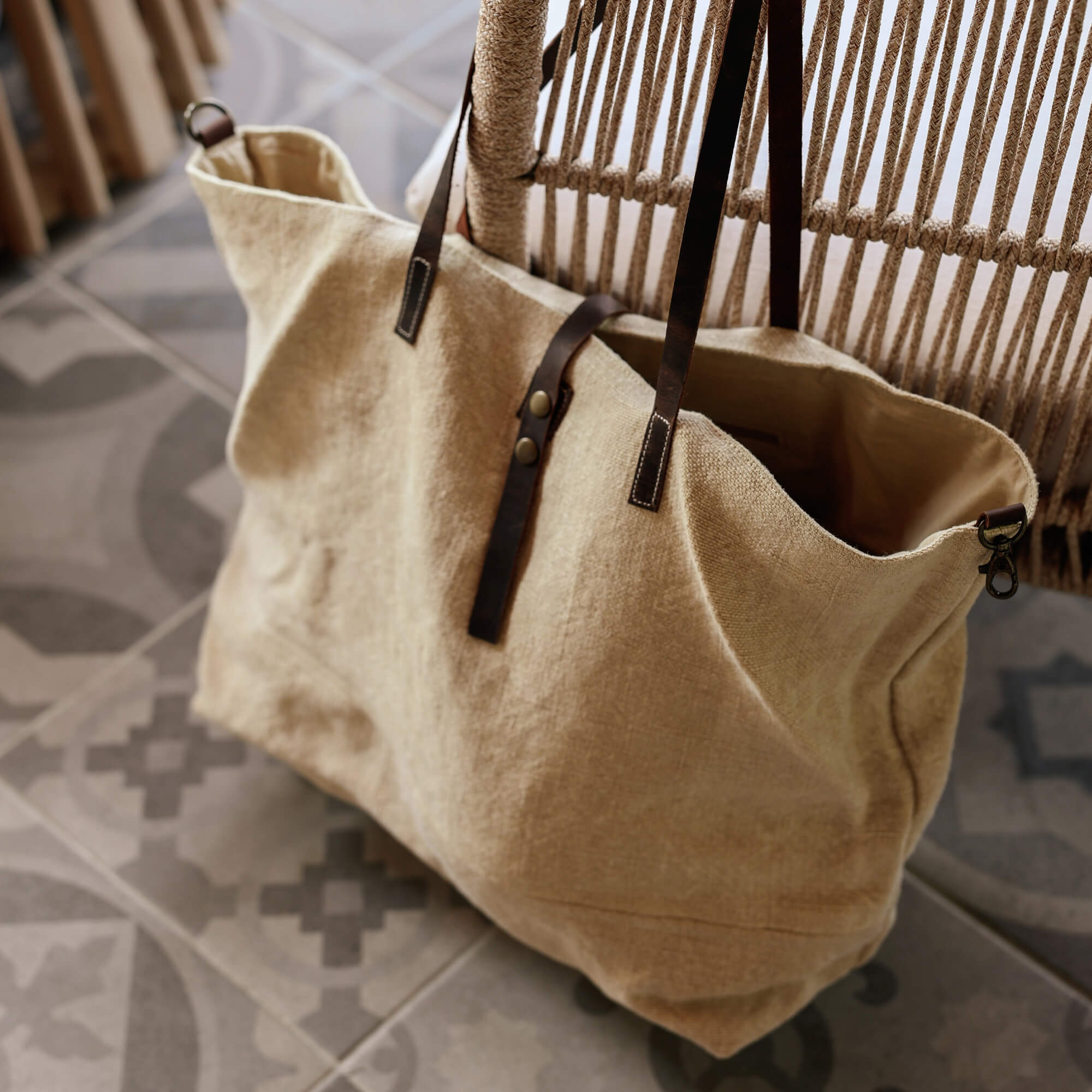 Borsa beige in tessuto con manici in pelle marrone scuro su pavimento piastrellato decorato