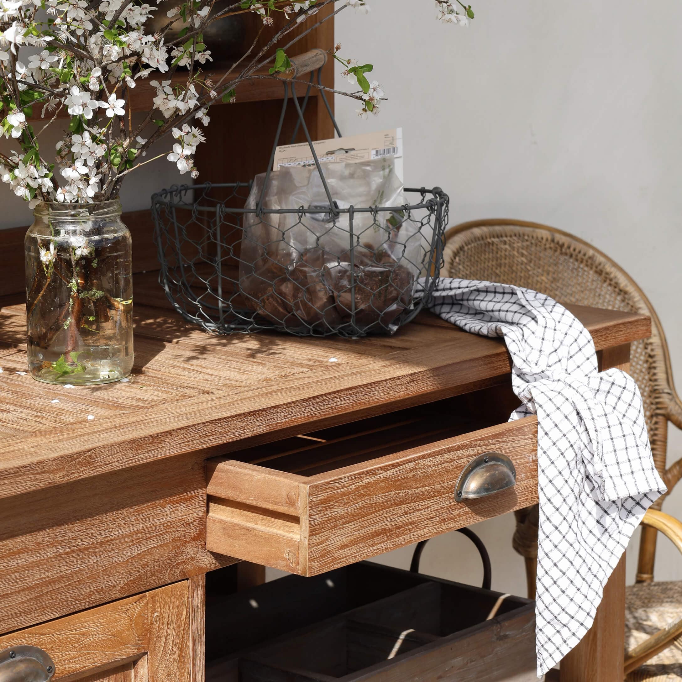 Tavolo in legno con cassetto aperto, cesta in metallo e strofinaccio bianco a quadri sul piano