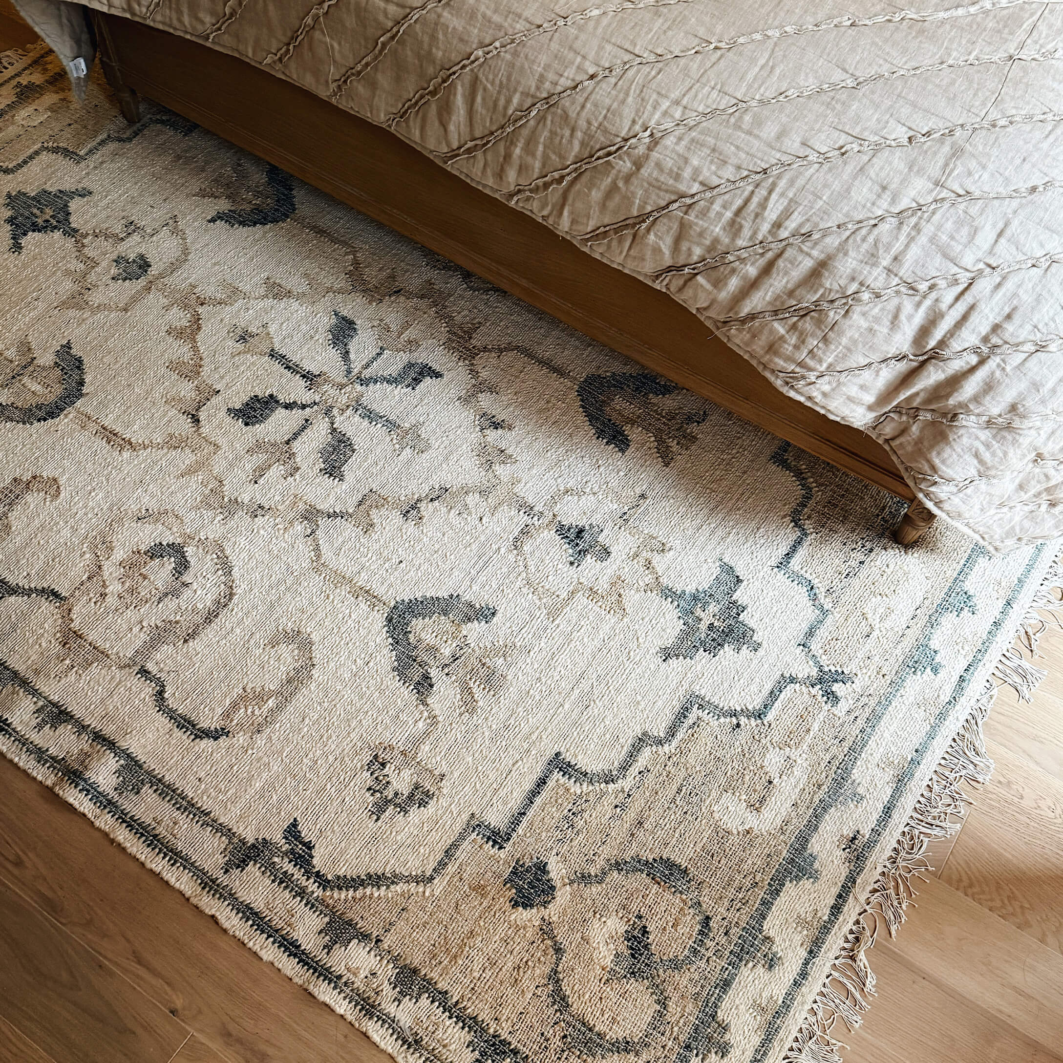 Tappeto beige con motivo orientale sotto il letto su pavimento in legno, decorazione d'interni
