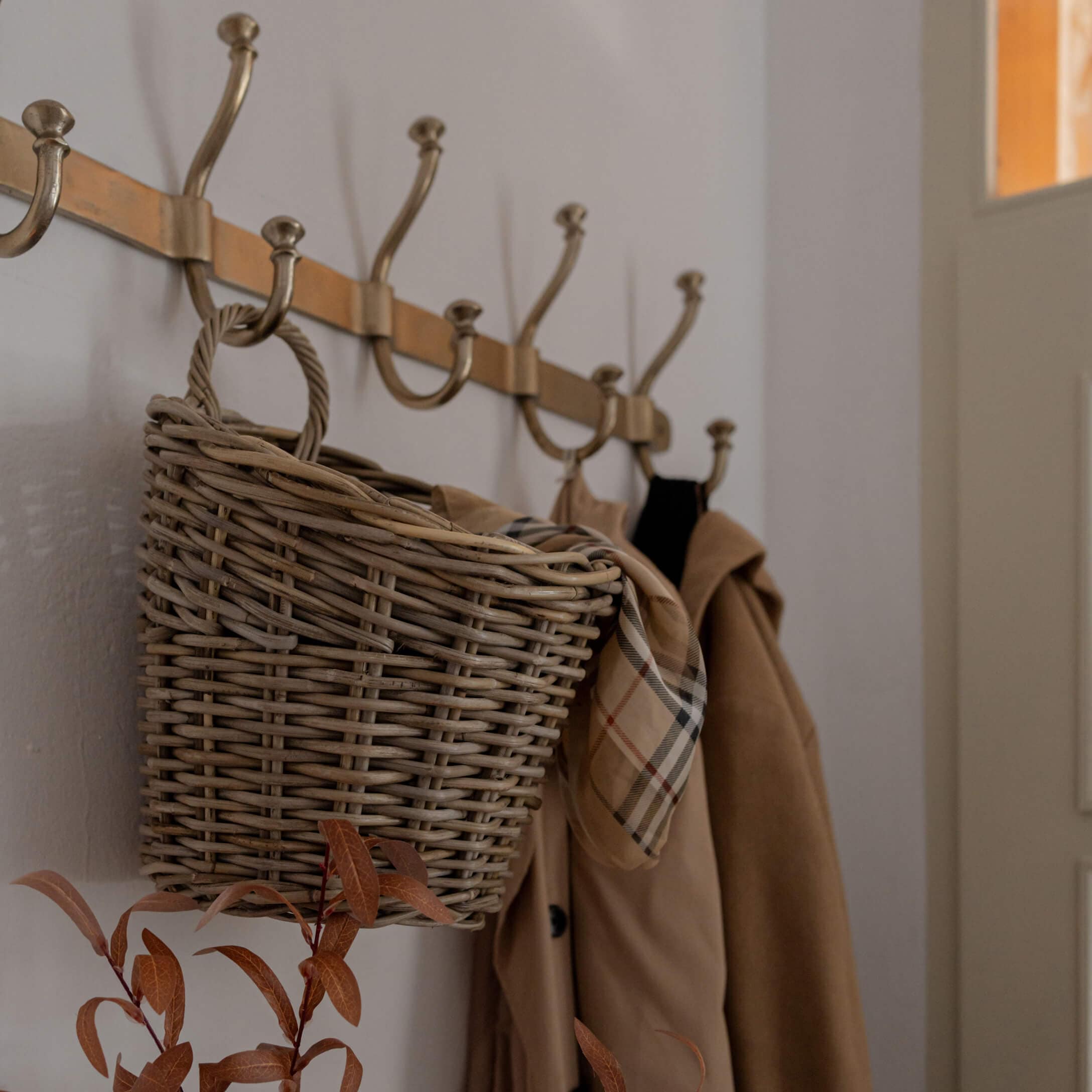 Cesto in vimini appeso a appendiabiti in ottone con cappotto beige e sciarpa a quadri