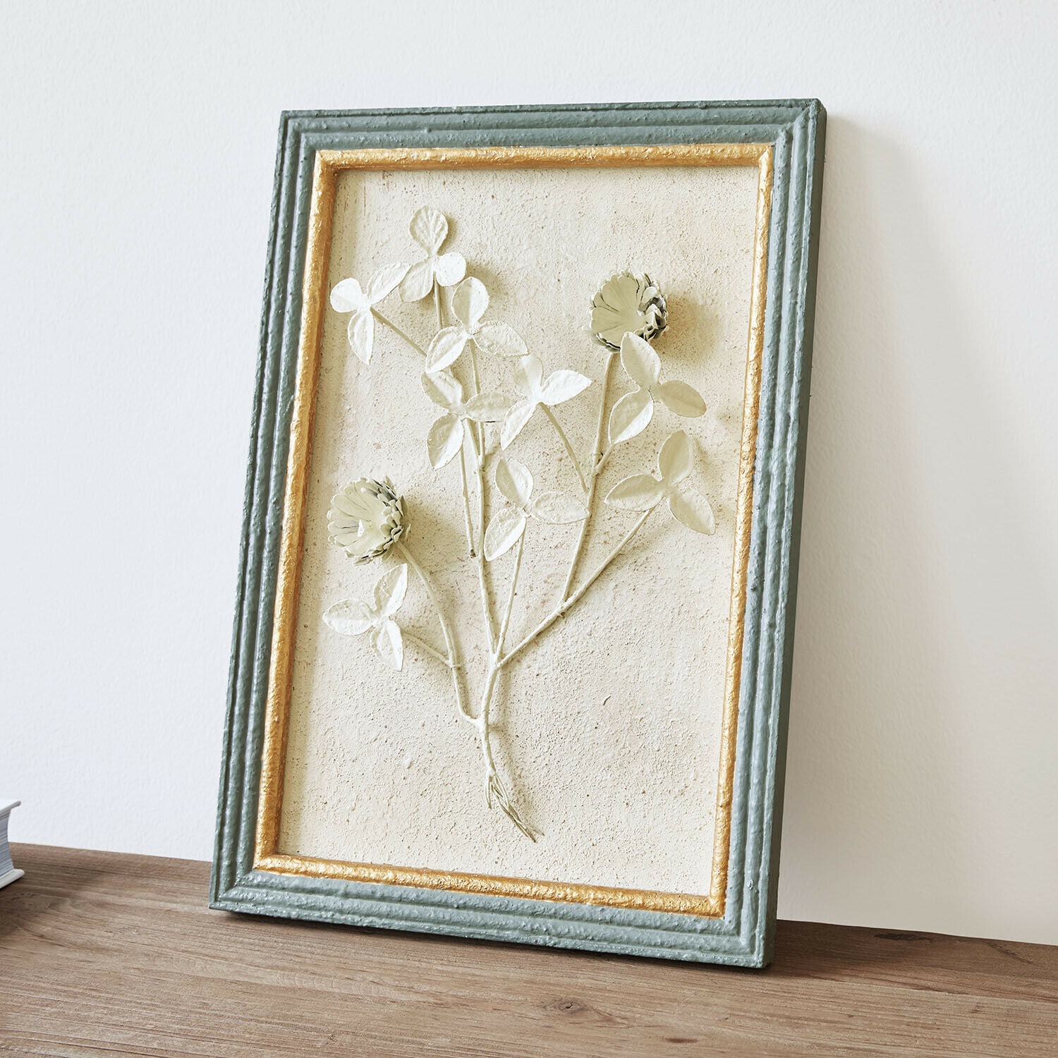 Quadro Rivolenne Quadro decorativo con rilievo floreale in cornice verde e dorata su tavolo in legno