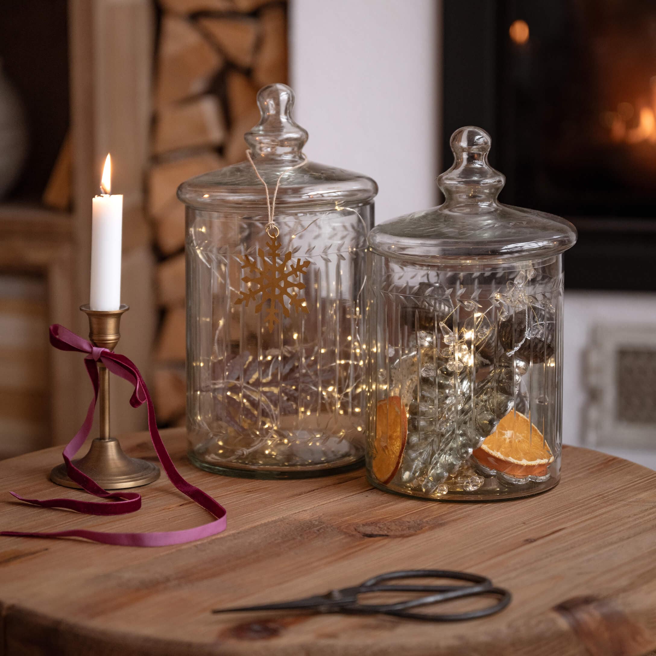 Barattoli di vetro trasparente con coperchi su tavolo in legno, decorati con luci e candela accesa