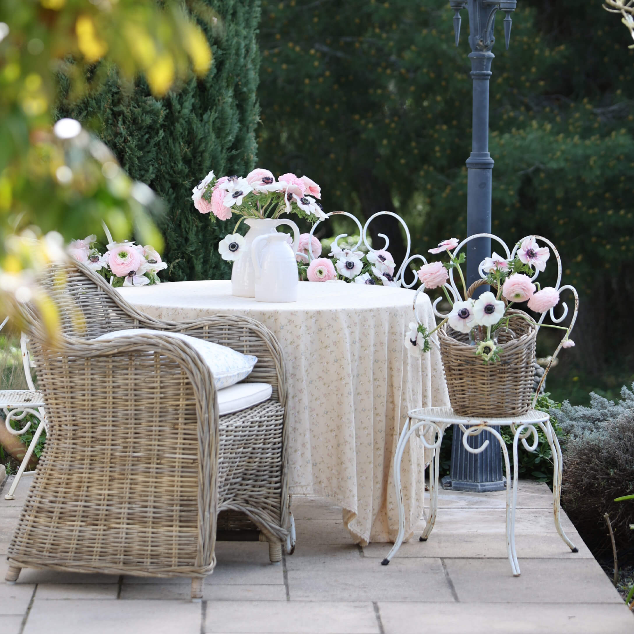 Giardino con poltrona in vimini, tavolo bianco con tovaglia e fiori in vasi, atmosfera romantica