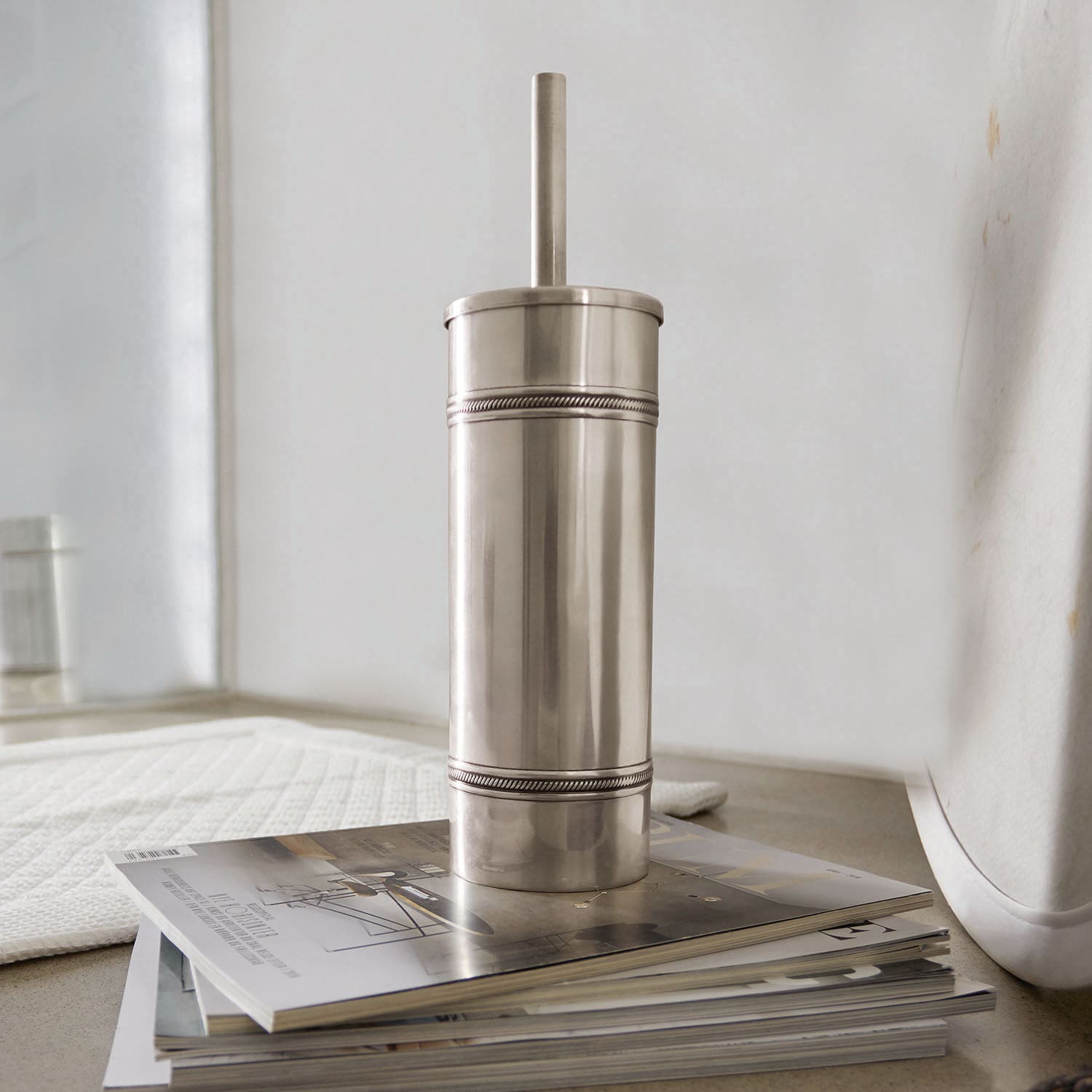 Scopino e portascopino da WC Semoine Contenitore metallico argentato con coperchio su una pila di riviste, decorazione bagno